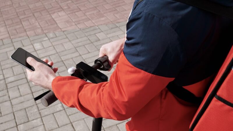 A delivery courier holding a smartphone while riding, checking the delivery app