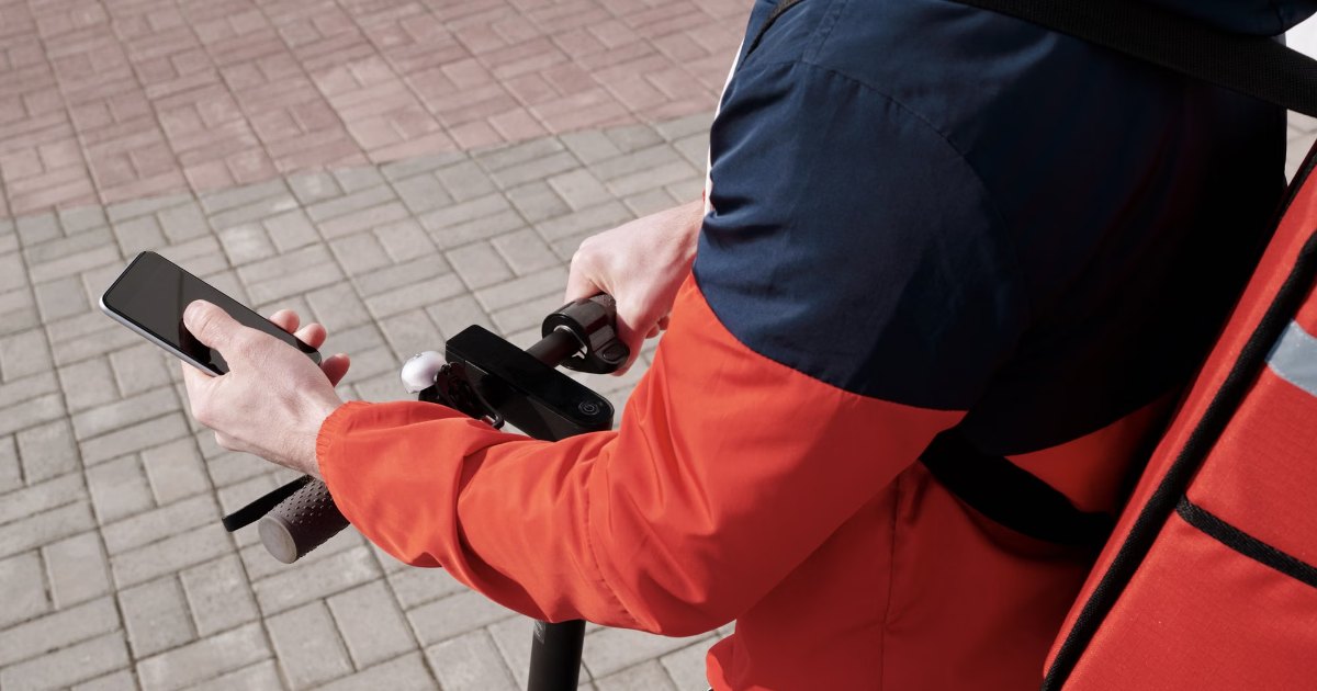 A delivery courier holding a smartphone while riding, checking the delivery app